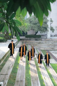 a group of children dressed in black and orange robes walking down a wooden walkway with trees behind them