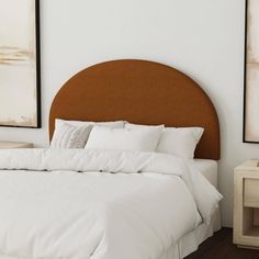 a bed with white linens and pillows in a small room next to two framed pictures on the wall