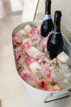 two bottles of beer are sitting in an ice bucket filled with flowers and cubes