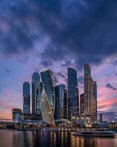 the city skyline is lit up at night with boats in the water and skyscrapers on either side