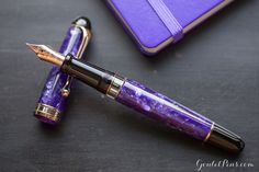 a purple pen sitting on top of a table next to a purple notebook and gold trimming