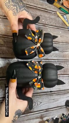 two hands are holding small black pumpkins with orange and yellow designs on them,