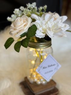 white flowers are in a mason jar with lights