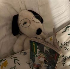 a stuffed dog wearing glasses reading a book on a bed with white sheets and pillows