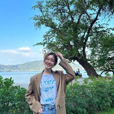 a woman standing in front of a tree with her hands on her head and smiling