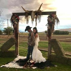 a bride and groom are standing under an arch decorated with flowers, feathers and skulls