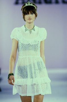 a woman walking down a runway wearing a white dress and headpiece with beads on it