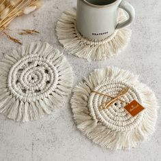 three coasters with tassels and a coffee cup on the table next to them