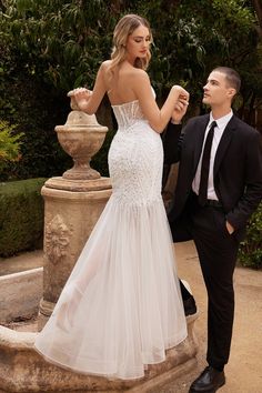 a man and woman standing next to each other in front of a fountain wearing formal attire