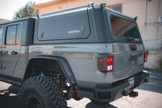 the rear end of a gray jeep parked in a parking lot next to a building