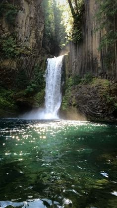 a large waterfall in the middle of a forest filled with green trees and blue water