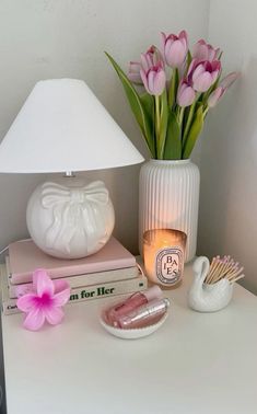 a white table topped with pink flowers next to a lamp and book on top of it