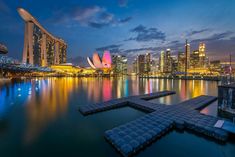 the city skyline is lit up at night with lights reflecting on the water and buildings in the background