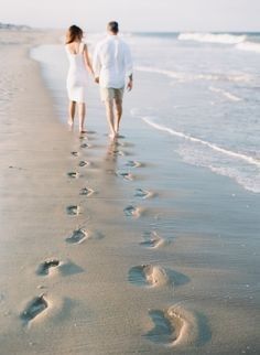 a man and woman walking on the beach with footprints in the sand as if they were holding hands