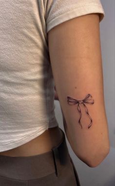 a woman's arm with a small bow tattoo on the back of her left arm