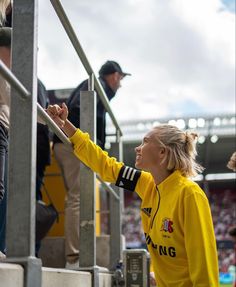 a woman in a yellow sweatshirt reaching up to grab something out of the bleachers