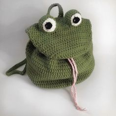 a crocheted green frog bag with eyes on it's side and a pink string