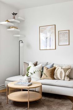 a living room with white couches and pillows on top of the sofa, next to a round coffee table