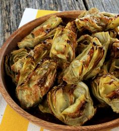 a wooden bowl filled with artichokes sitting on top of a yellow and white table cloth