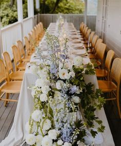 a long table with white and blue flowers is set up for an outdoor dinner party