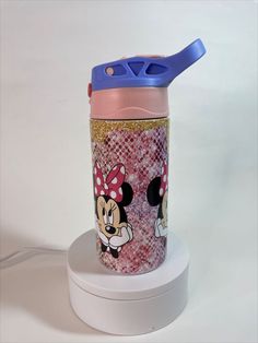 a pink and blue cup with minnie mouse on it sitting on a white stand next to a plastic container