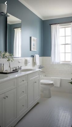 a bathroom with blue walls and white fixtures, including a tub, toilet, sink, and window