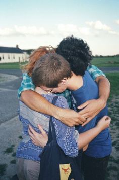 two people hugging each other in front of a field with grass and houses behind them