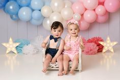 two babies sitting on a chair in front of balloons