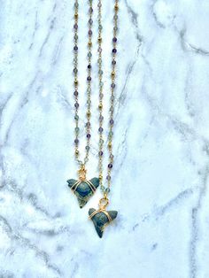 two necklaces on a marble surface with gold and blue beads hanging from the chain