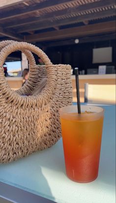 a straw bag sitting on top of a table next to a glass filled with liquid