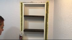 a woman standing in front of a white wall with shelving on it's sides