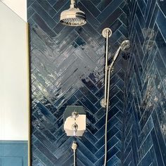 a shower head and hand shower in a blue tiled bathroom with herringbone tiles on the wall