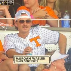 a baseball player sitting in the dugout holding a sign that says morgan wallen sings songwriter