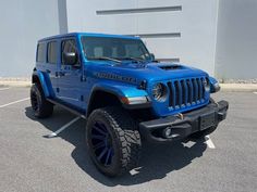 a blue jeep parked in a parking lot next to a white building with black lettering on it