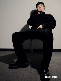 a man sitting on top of a chair wearing a black hat and sweater with his hand under his chin