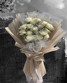 a bouquet of white roses wrapped in brown paper and tied to a postcard holder