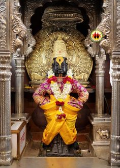 the statue is dressed in yellow and pink with flowers on it's chest, sitting next to a golden wall