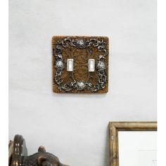 an ornate light switch plate on a white wall with a wooden frame in the corner