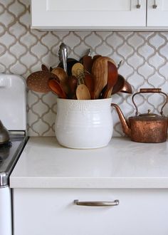 a white kitchen counter topped with a tea kettle and pot filled with cooking utensils