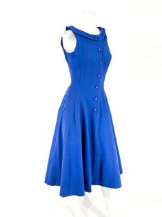 For Sale on 1stDibs - 1960s blue wool dress fitted to the waist with a flared skirt. The face of the dress has a button closure the goes down past the hip. The sides are adorned Classic Blue Dress For Vintage Fashion, Blue Vintage Dress With Buttons For Vintage Fashion, Blue Vintage Dress With Buttons, Blue A-line Dress With Buttons, Fitted A-line Vintage Dress With Buttons, Blue A-line Vintage Fashion Dress, 1950s Style A-line Vintage Dress With Buttons, 1950s A-line Dress With Buttons, A-line Vintage Dress With Buttons