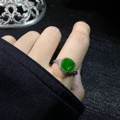 a person wearing a ring with a green stone on it's middle finger, next to a silver object