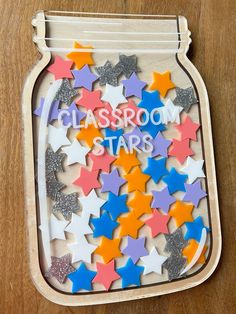 a glass jar filled with colorful stars on top of a wooden table next to a sign that says classroom stars