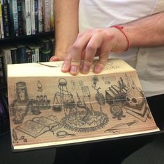 a person holding a box with drawings on it in front of a book shelf filled with books