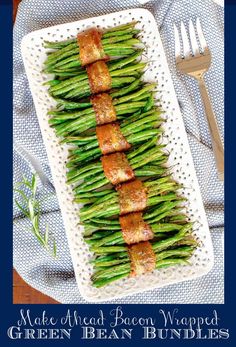 asparagus wrapped in bacon on a white platter next to a fork and knife