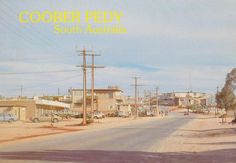 an old photo of a town with cars parked on the side of the road and telephone poles in the foreground