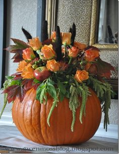 an orange pumpkin filled with flowers on top of a wooden table next to a mirror