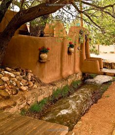 an adobe - style house with potted plants on the wall and water running through it