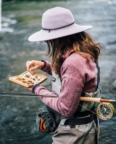 a woman standing in the water holding a fishing rod and a box with food on it