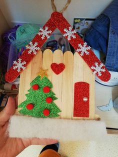 a hand holding a wooden house with a christmas tree on it