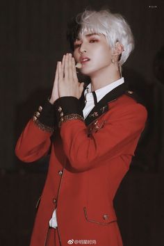 a man with white hair wearing a red suit and holding his hands to his face